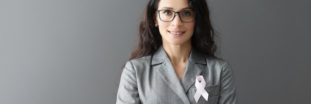 Portrait of smiling woman in gray suit on her chest with pink\
ribbon symbol of fight against