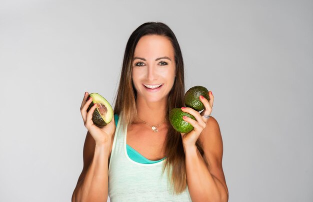 Foto ritratto di una donna sorridente che tiene un avocado sullo sfondo grigio