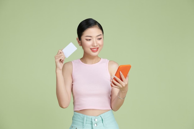 Portrait of a smiling woman holding credit card and mobile phone over green