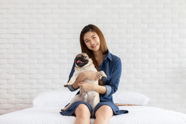 家のベッドに座っている犬を抱いた笑顔の女性の肖像画
