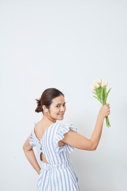 Portrait of smiling woman holding flowers while standing against white background