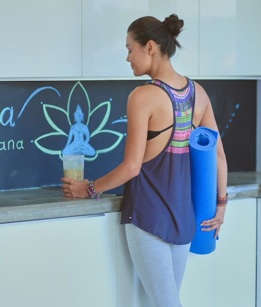 Portrait of smiling woman holding in her hand a yoga mat while\
standing at studio yoga woman wellness