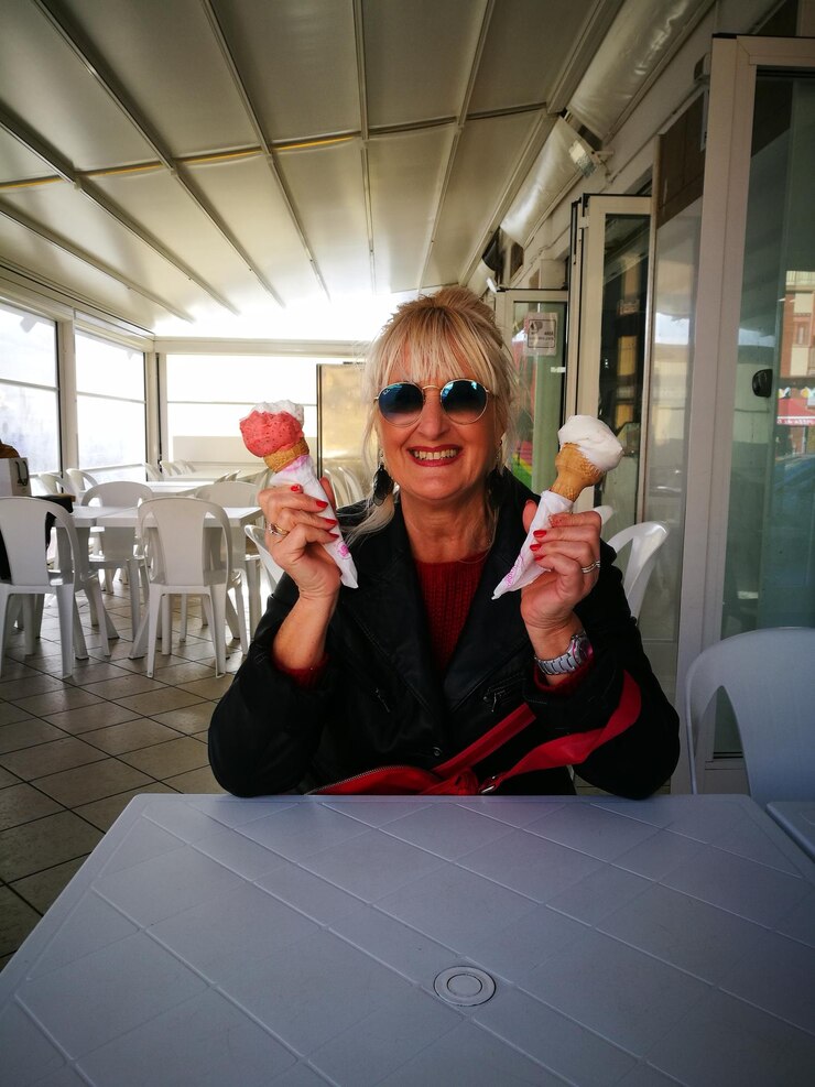 Photo portrait of smiling woman holding ice cream cones while sitting at table