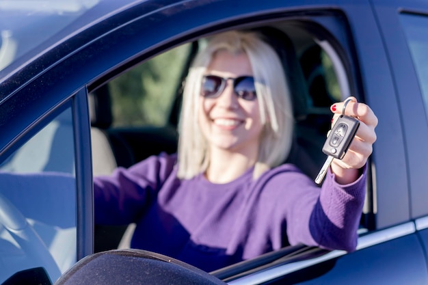 Photo portrait of smiling woman holding key while sitting in car