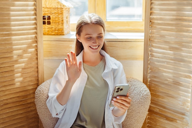 携帯電話を握っている笑顔の女性の肖像画オンライン通信手を振ってビデオコールをしている