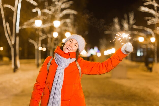 Foto ritratto di una donna sorridente che tiene in mano una scintilla durante l'inverno