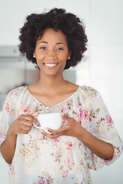 Portrait of smiling woman holding white cup in the kitchen