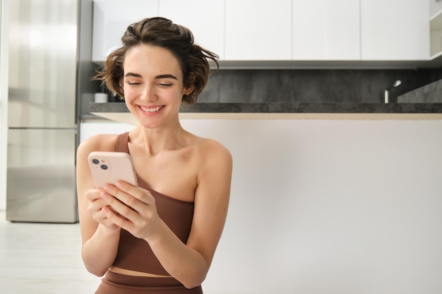 Portrait of smiling woman at home using her mobile phone sitting on floor in bright room looking at