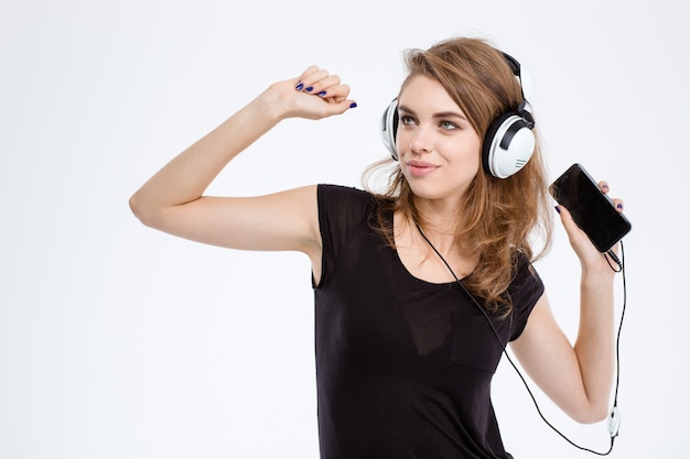 Portrait of a smiling woman listening the music in headphones on smartphone isolated on a white background