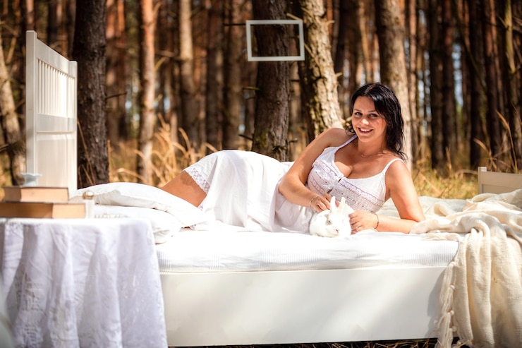 Photo portrait smiling woman lying on bed with rabbit in forest