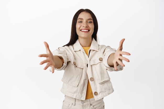 Portrait of smiling woman reaching for hugs, taking something, stretching hands forward with cute and tender facial expression, receiving smth on white