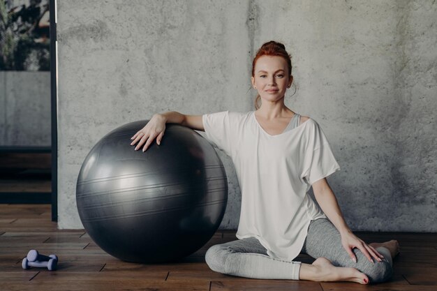 Portrait of smiling woman sitting by fitness ball at gym
