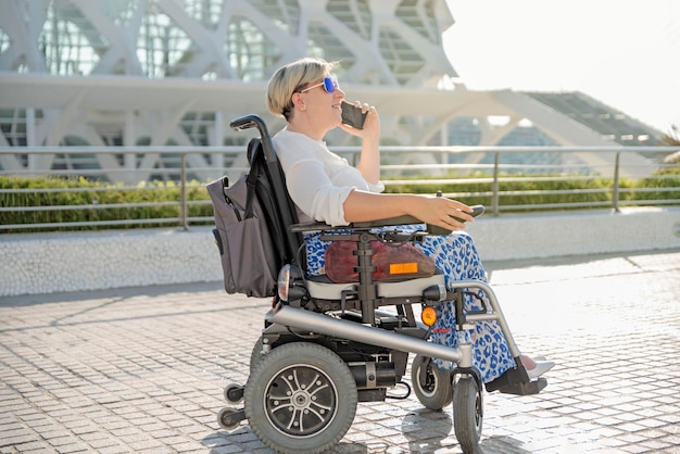 Портрет улыбающейся женщины, сидящей в электрической инвалидной коляске и разговаривающей по мобильному телефону