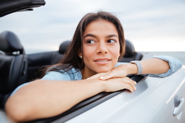 ビーチで彼女のコンバーチブル車に座っている笑顔の女性の肖像画