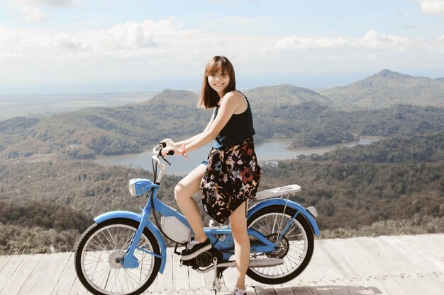 Foto ritratto di una donna sorridente seduta su una moto contro la catena montuosa