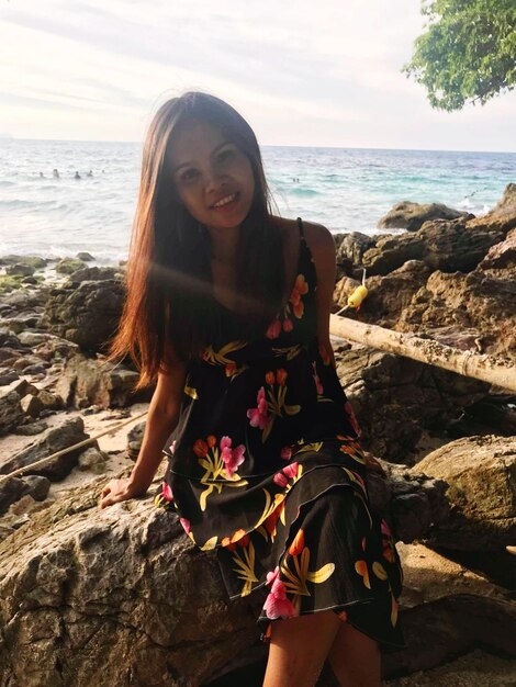 Portrait of smiling woman sitting on rock at beach