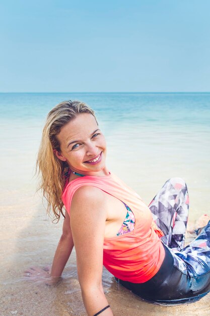 Portrait of smiling woman sitting on shore against sea at beach