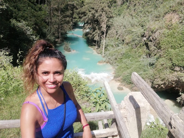 Foto ritratto di una donna sorridente in piedi contro il ruscello nella foresta