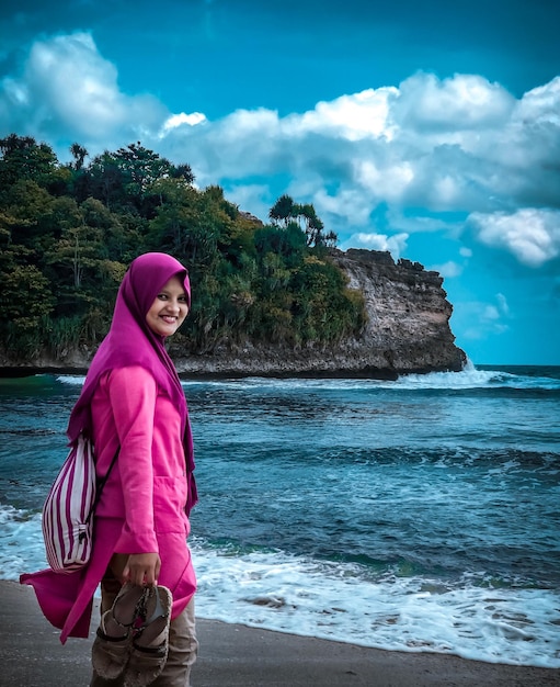 Portrait of smiling woman standing on beach by sea against sky