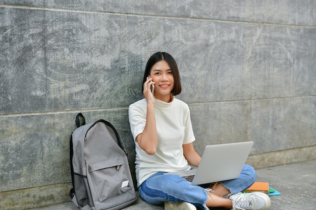 Photo portrait of smiling woman talking on mobile phone while using laptop