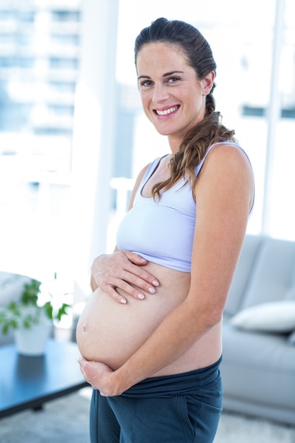 Portrait of smiling woman touching belly while standing 