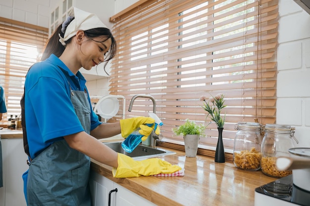 Portrait of smiling woman in uniform cleaning kitchen worktop with spray and cloth housekeeping emphasizing hygiene and safety cleaning routine for a purified home clean disinfect home care