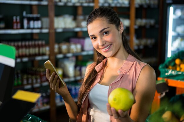 Portrait of smiling woman using her phone while buying fruits in organic section