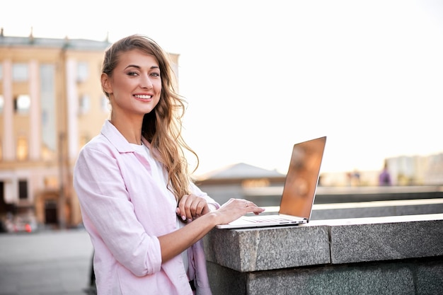 Foto ritratto di una donna sorridente che usa un portatile su un muro di supporto