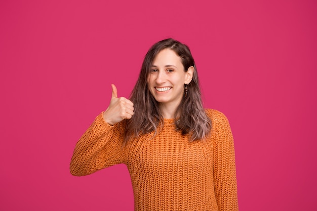 Ritratto della donna sorridente che porta maglione giallo e che mostra i pollici in su