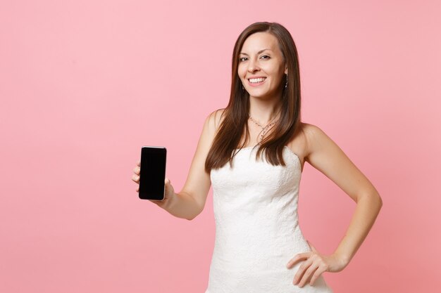 Портрет улыбающейся женщины в белом платье, держащей мобильный телефон с пустым черным экраном