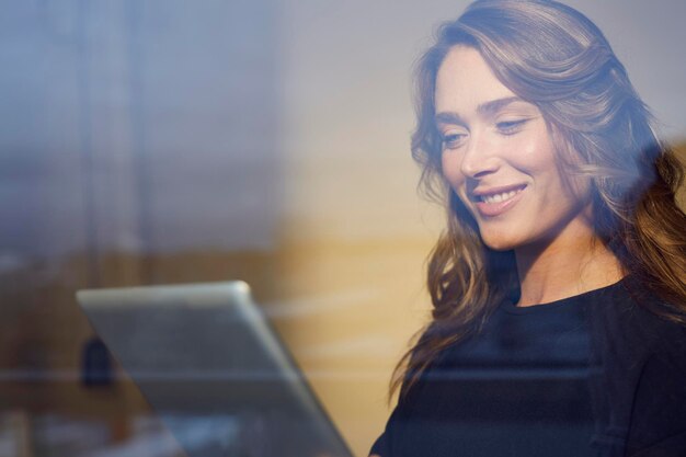 Portrait of smiling woman behind windowpane using tablet