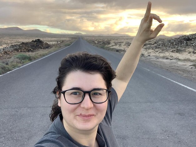 Foto ritratto di una donna sorridente con le braccia alzate che mostra un segno di pace sulla strada