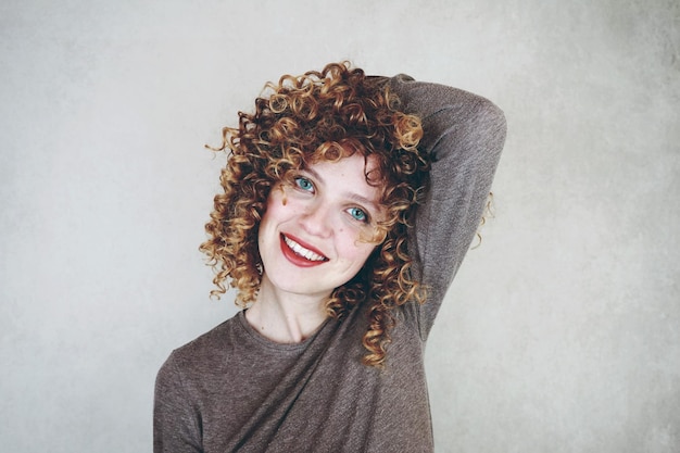 Photo portrait of smiling woman with curly hair against wall