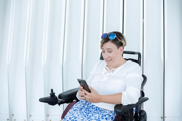 Portrait of a smiling woman with disability in a wheelchair looking at her smartphone on a white background