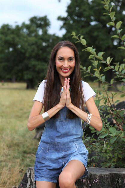 Foto ritratto di una donna sorridente con le mani giunte seduta sul tronco di un albero