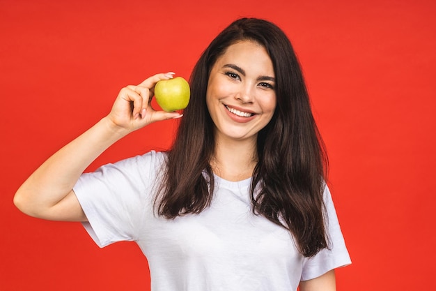 Portrait of smiling woman with healthy teeth holding green apple Isolated over red background