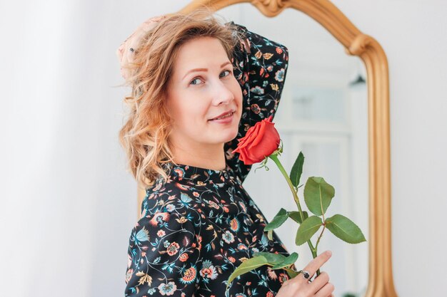 Foto ritratto di una donna sorridente con una rosa contro lo specchio a casa