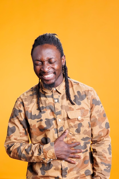 Portrait of smiling young adult laughting during studio shot, laughting at camera over yellow background. African american relaxed person having positive facial expression, posing confident