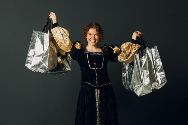 Portrait of a smiling young adult woman dressed in a medieval dress holding shopping bags in hands