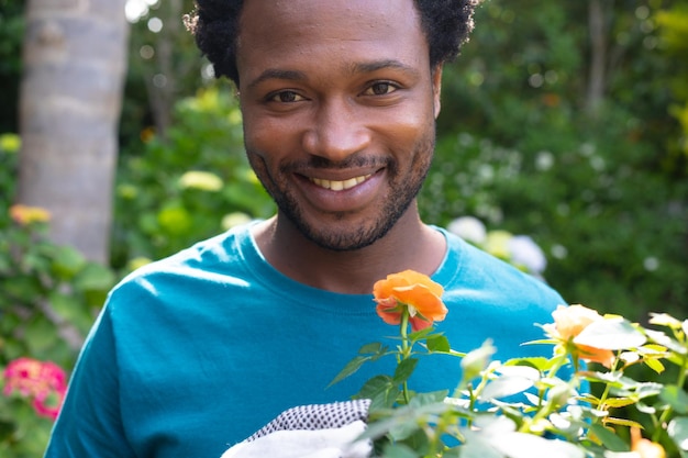 뒷마당에서 정원을 가꾸는 동안 꽃식물을 들고 웃고 있는 젊은 아프리카계 미국인의 초상화
