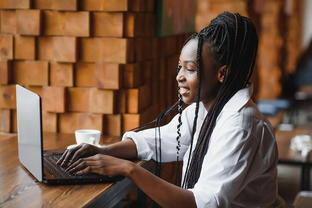 노트북으로 카페에 앉아 웃고 있는 젊은 아프리카계 미국인 여성의 초상화