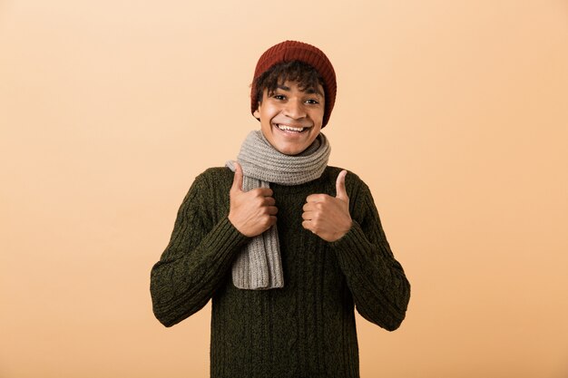 Portrait of a smiling young african man dressed in autumn clothes isolated over beige wall, giving thumbs up