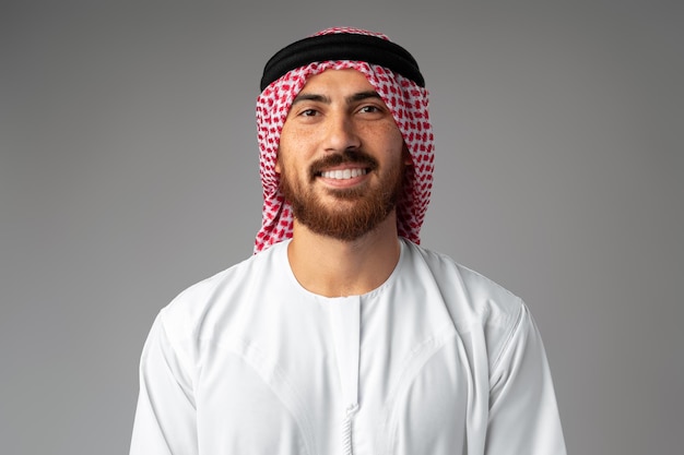 Portrait of smiling young Arab man on gray background