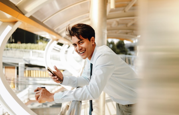 Portrait of a Smiling Young Asain Businessman Using Mobile Phone in the City