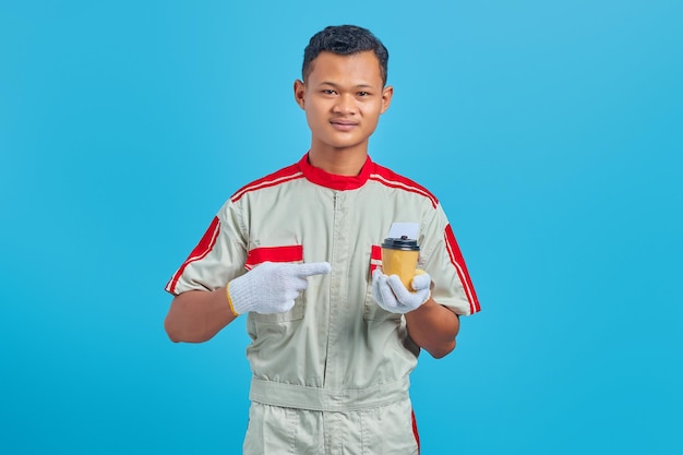 Portrait of smiling young Asian mechanic carrying cup of coffee in hand over blue background