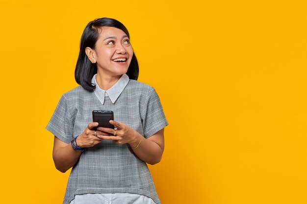 Portrait of smiling young asian woman holding cell phone and looking aside