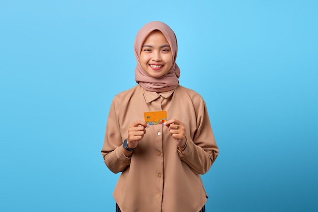 Portrait of smiling young Asian woman holding credit card while looking at camera