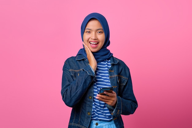 Портрет улыбающейся молодой азиатской женщины, держащей мобильный телефон с рукой на щеках