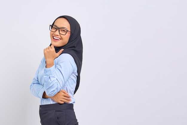 Portrait of smiling young Asian woman pointing thumbs at copy space isolated on white background