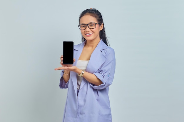 Portrait of smiling young Asian woman showing blank screen phone with palm isolated on white background